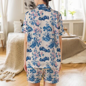 May include: Cream-colored pajama set with a blue and pink floral and race car pattern. The short-sleeved top and shorts have blue trim. The fabric features a toile design with trees, flowers, and race cars.