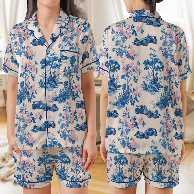 May include: Cream-colored pajama set with a blue and pink floral and race car pattern. The set includes a short-sleeved button-down shirt and matching shorts, both trimmed with navy blue piping.