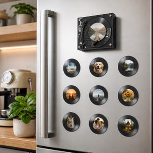 Könnte beinhalten: Eine Sammlung schwarzer Schallplattenmagnete mit verschiedenen Landschafts- und Porträtbildern, darunter ein Hund, Sonnenblumen und eine Strandszene. Ein schwarzer Plattenspielermagnet ist ebenfalls an einem Kühlschrank aus Edelstahl angebracht.