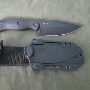 May include: A black knife with a fixed blade and a matching sheath. The knife has a dark handle and the text "BK-18" is visible on the blade. The sheath includes a black belt loop.