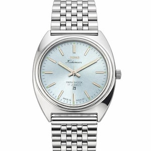 Może przedstawiać: Srebrny zegarek z jasnoniebieską tarczą i pasującą metalową bransoletą. Tarcza zegarka zawiera napisy "Kohinoor" i "Para Shock 17 Jewels". Zegarek posiada wyświetlacz daty. Wyprodukowano w Indiach.