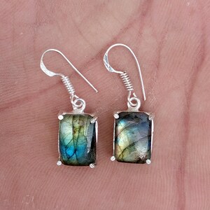 May include: A pair of drop earrings featuring rectangular labradorite gemstones with iridescent blue and gold flashes. The stones are set in silver-toned metal settings with four prongs each and attached to silver-toned shepherd hook ear wires.