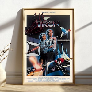 May include: A framed movie poster for the film "Tron." The poster features a futuristic design with the title in a bold, neon-style font. The artwork includes images of characters in glowing suits and vehicles, with the tagline "A Real Adventure in an Electronic World."