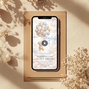 May include: A smartphone screen shows a baby shower invitation. The design includes a teddy bear with blue and beige balloons. The text reads "We can bearly wait" and event details, including the date and time.