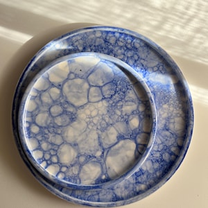May include: Two round ceramic plates with a blue and white bubble pattern. The plates are nested, with a smaller plate inside a larger one. The design features a network of interconnected, irregular shapes in shades of blue against a white background.