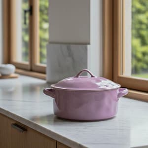 May include: A light purple ceramic cooking pot with a lid and two side handles, set on a white countertop. The pot has a rounded shape and a loop handle on the lid. The background includes a window and wooden cabinetry.
