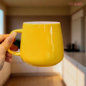 May include: A vibrant yellow ceramic mug with a white interior. The mug features a rounded design and a curved handle. The brand name "quinNora" is visible in the top right corner. Ideal for tea, coffee, or any hot drink.