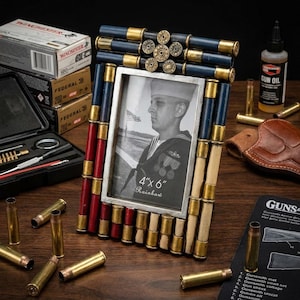 Puede incluir: Un marco de fotos único, de aproximadamente 10x15 cm, decorado con casquillos de bala y pintado en rojo, blanco y azul. El marco contiene una foto en blanco y negro de un marinero. Se ven casquillos adicionales y aceite para armas.