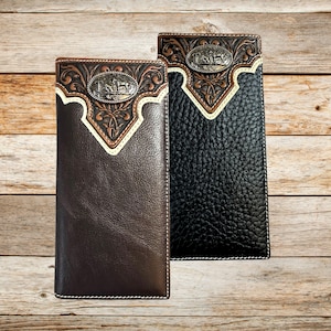 May include: Two leather wallets, one brown and one black, with decorative metal accents. The wallets feature a detailed embossed design with a silver-colored emblem. The brown wallet has a smooth texture, while the black wallet has a textured surface.