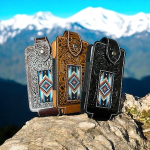 Puede incluir: Tres fundas de teléfono de cuero con intrincados diseños florales y geométricos. Las fundas son plateadas, marrones y negras, cada una con un patrón de cuentas en el centro con acentos azules, rojos y blancos. Las fundas tienen un cierre de solapa.