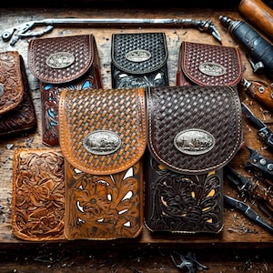 Peut inclure: Plusieurs étuis de téléphone en cuir faits à la main, de couleurs marron et noir. Chaque étui présente un emblème métallique décoratif et des motifs tissés ou floraux complexes. Les étuis sont conçus avec une fermeture à rabat et sont exposés sur une surface en bois.