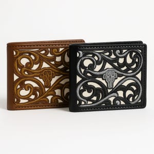 Puede incluir: Dos carteras de cuero con intrincados diseños de volutas y un diseño central de calavera de toro. Una cartera es marrón con detalles en beige, la otra es negra con detalles plateados. Ambas tienen un diseño plegable.