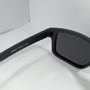 May include: Black sunglasses with rectangular frames. The left arm of the sunglasses has the numbers "009244 56 17-138" printed on it. The lenses are dark, and the frames are matte black.
