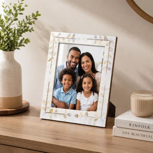 May include: A rectangular picture frame featuring an inlaid mother-of-pearl border with a delicate leaf pattern in shades of white and iridescent gold. The frame holds a photograph of a family of four, including two adults and two children.