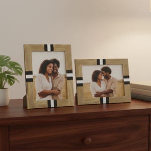 Op de afbeelding: Twee houten fotolijsten met zwart-witte accenten. Elke lijst bevat een foto van een stel. De lijsten worden weergegeven op een donkerbruin houten oppervlak.