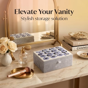 May include: A gray velvet jewelry box with a beaded floral design in blue and white sits on a marble surface. The box is next to a gold-framed mirror, perfume, and a makeup brush. The text "Elevate Your Vanity" and "Stylish storage solution" is visible.