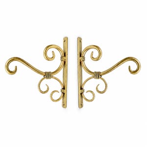May include: A pair of gold-toned metal wall brackets featuring a vertical mounting plate and decorative scrollwork arms. Each bracket has three distinct curled elements and wrapped metal detailing at the joints, designed for wall mounting.