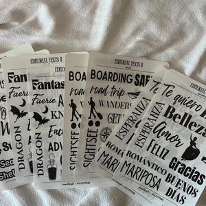 May include: A collection of rectangular, translucent sticker sheets featuring black printed text and icons. The sheets include words like Fantasy, Dragon, Boarding, Esperanza, and Te quiero, alongside graphics of bats, compasses, and silhouettes.