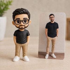 May include: A custom bobblehead figurine of a person with dark hair, a beard, and black-rimmed glasses, wearing a black t-shirt, tan pants, and white sneakers, displayed next to a rectangular photo print of the same person in identical clothing.