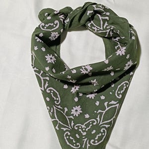 Puede incluir: Bandana verde oliva con un estampado floral y paisley en rosa claro. La bandana está doblada y anudada, mostrando el diseño. Este accesorio se puede usar como pañuelo en la cabeza o pañuelo para el cuello.