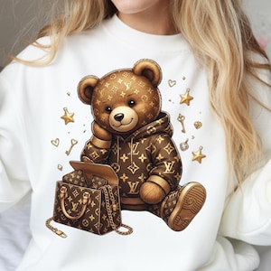Peut inclure: Un ours en peluche marron portant un sweat à capuche et des chaussures marron, avec un sac à main assorti. L'ours est orné d'un motif répétitif. Des étoiles, des clés et des cœurs dorés sont dispersés autour de l'ours. L'ours est assis sur une surface blanche.