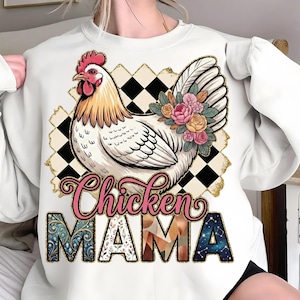 May include: White sweatshirt featuring a detailed illustration of a chicken with floral accents on its wing. The design includes the text "Chicken MAMA" in a decorative font. The background has a black and white checkered pattern with gold accents.