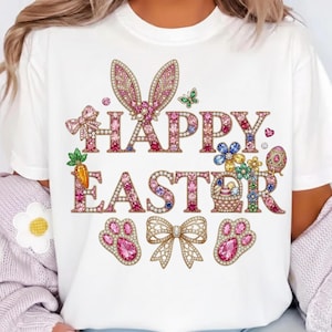 May include: White t-shirt with a colorful "HAPPY EASTER" graphic. The design features bunny ears, flowers, a basket, and paw prints, all embellished with pink and jewel-toned accents. A bow and a butterfly are also included in the design.