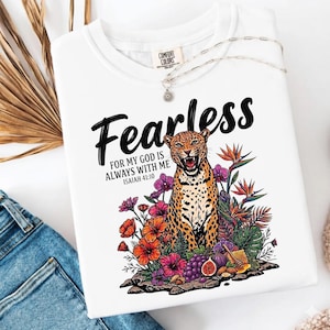 Może przedstawiać: Biała bluza Comfort Colors z grafiką przedstawiającą lamparta, kwiaty i słowo "Fearless". Tekst "For my God is always with me Isaiah 41:10" jest również dołączony. Srebrny naszyjnik jest zarzucony na koszulę.