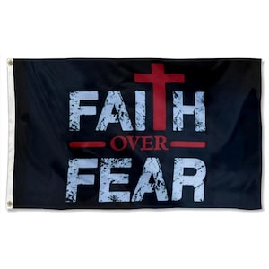 Może przedstawiać: Czarna flaga z białym, postarzanym tekstem „FAITH OVER FEAR”. Czerwony krzyż znajduje się nad słowem „FAITH”, a czerwona linia podkreśla słowo „OVER”. Flaga ma białe przelotki po lewej stronie.