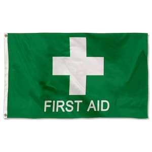 May include: A green flag featuring a white cross and the words "FIRST AID" in white. The flag is rectangular with eyelets on the left edge for hanging. The design is a universal symbol for medical assistance.