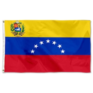 Op de afbeelding: Een rechthoekige vlag met de kleuren geel, blauw en rood. De bovenkant is geel, het midden is blauw met zeven witte sterren en de onderkant is rood. Een wapenschild is zichtbaar in de linkerbovenhoek.