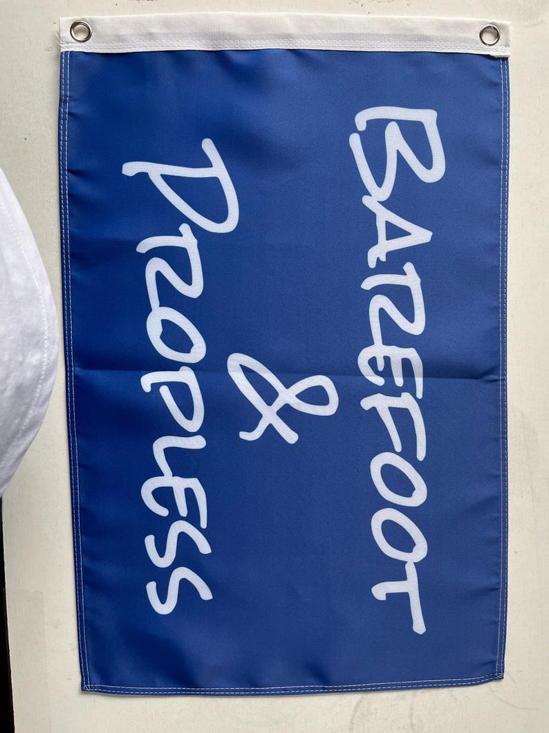 Pode incluir: Uma bandeira azul com texto branco "Barefoot & Progress". A bandeira tem uma borda branca na parte superior com dois ilh&oacute;s de metal. A bandeira est&aacute; pendurada em uma parede.