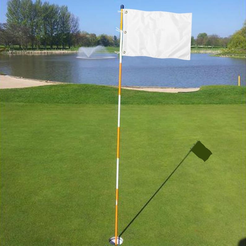Pu&ograve; includere: Una bandiera da golf bianca tinta unita fissata a un'asta alta e sottile con strisce orizzontali alternate arancioni e bianche. L'asta &egrave; inserita in un foro circolare nell'erba verde, con la bandiera che si estende orizzontalmente a destra.