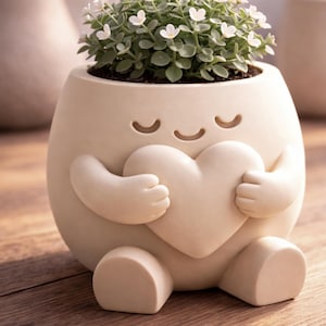 Peut inclure: Un pot de fleurs fantaisiste de couleur crème en forme de personnage embrassant un cœur. Le pot contient une petite plante avec des feuilles vertes et de minuscules fleurs blanches. Le design présente des yeux fermés, des bras et des jambes.