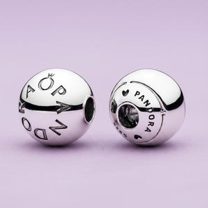 Puede incluir: Dos abalorios Pandora plateados. Uno tiene la palabra "Pandora" y una corona grabada. El otro tiene la palabra "Pandora" y un corazón grabado. Ambos abalorios tienen una superficie brillante y reflectante.