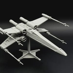 May include: A light gray X-wing starfighter model, a spacecraft with distinctive wings and four engines. The model is mounted on a stand, set against a dark background. The wings are in an X-shape.