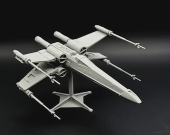 Puede incluir: Maqueta de un caza estelar X-wing gris claro, una nave espacial con alas distintivas y cuatro motores. El modelo está montado sobre un soporte, sobre un fondo oscuro. Las alas tienen forma de X.