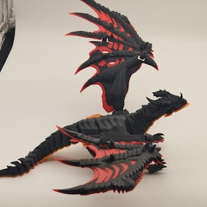 Op de afbeelding: Een zwarte drakenfiguur met rode details op de vleugels en het lichaam. De draak wordt afgebeeld met uitgespreide vleugels, met ingewikkelde details en een dynamische pose. Dit beeldje is waarschijnlijk een verzamel- of decoratie-artikel.