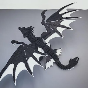Op de afbeelding: Een zwart-witte gearticuleerde drakenfiguur met een gesegmenteerd lichaam, een lange staart en grote, gedetailleerde vleugels. De draak heeft een scherp, hoekig kopontwerp en ingewikkelde schubpatronen over de gehele structuur in een hoog contrast.