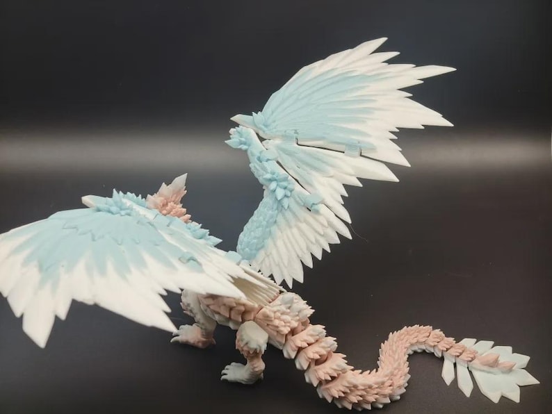 May include: A detailed figurine of a mythical creature with large, feathered wings. The wings are primarily white with light blue accents. The body is a mix of light pink and beige, with a textured, scaled appearance. The creature has a long, segmented tail.