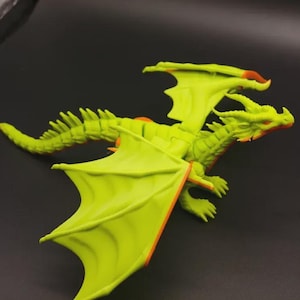 Può includere: Statuetta di drago verde lime con dettagli arancioni sulle ali e sulla testa. Il drago ha una lunga coda e grandi ali spiegate. La statuetta è ambientata su uno sfondo scuro.