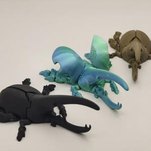 Puede incluir: Tres modelos de escarabajos impresos en 3D en negro, azul-verdoso y marrón. El escarabajo negro tiene grandes mandíbulas. El escarabajo azul-verdoso tiene las alas abiertas. El escarabajo marrón tiene un hocico largo. Todos tienen múltiples patas.