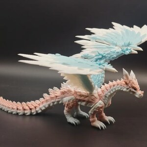 May include: A detailed figurine of a dragon with a white, light blue, and pink color scheme. The dragon has large, detailed wings and a long tail. The figurine is posed on a dark surface.