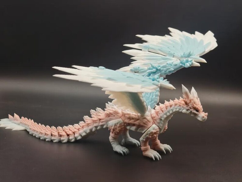May include: A detailed figurine of a dragon with a white, light blue, and pink color scheme. The dragon has large, detailed wings and a long tail. The figurine is posed on a dark surface.