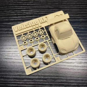 Op de afbeelding: Een beige plastic modelautokit met de tekst "Veilside RK7" op de gietboom. De kit bevat een carrosserie, wielen en andere onderdelen. De onderdelen zijn gerangschikt op een beige plastic frame.