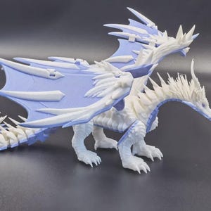 May include: A white and light blue articulated dragon figurine featuring a detailed head with horns, large wings with sharp edges, and a segmented tail. The creature is depicted in a standing position with visible joints along its body and limbs.