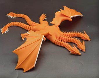 May include: An orange, three-headed dragon figurine with outstretched wings and multiple tails. The wings and tail tips have white accents. The dragon is posed on a dark gray surface.