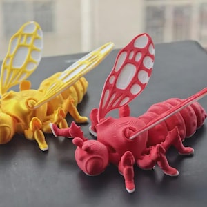 May include: Two 3D-printed insect models. One is yellow with white wings, the other is red with white accents on the wings. The insects have detailed legs, antennae, and segmented bodies, suggesting a bee or wasp theme.