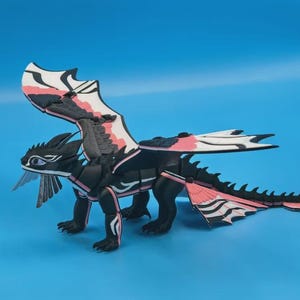 Op de afbeelding: Een zwart, wit en roze gearticuleerd drakenfiguur met grote vleugels, een lange gesegmenteerde staart en gedetailleerde gelaatstrekken. Het wezen staat op vier poten en heeft een strak, meerkleurig ontwerp met scherpe, gedefinieerde randen.