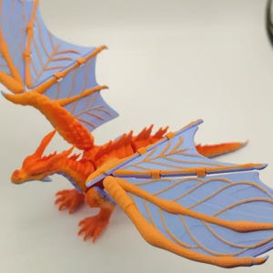 May include: A detailed orange and blue dragon figurine with outstretched wings. The dragon has a spiky back, orange claws, and a long tail. The wings are light blue with orange vein-like details.